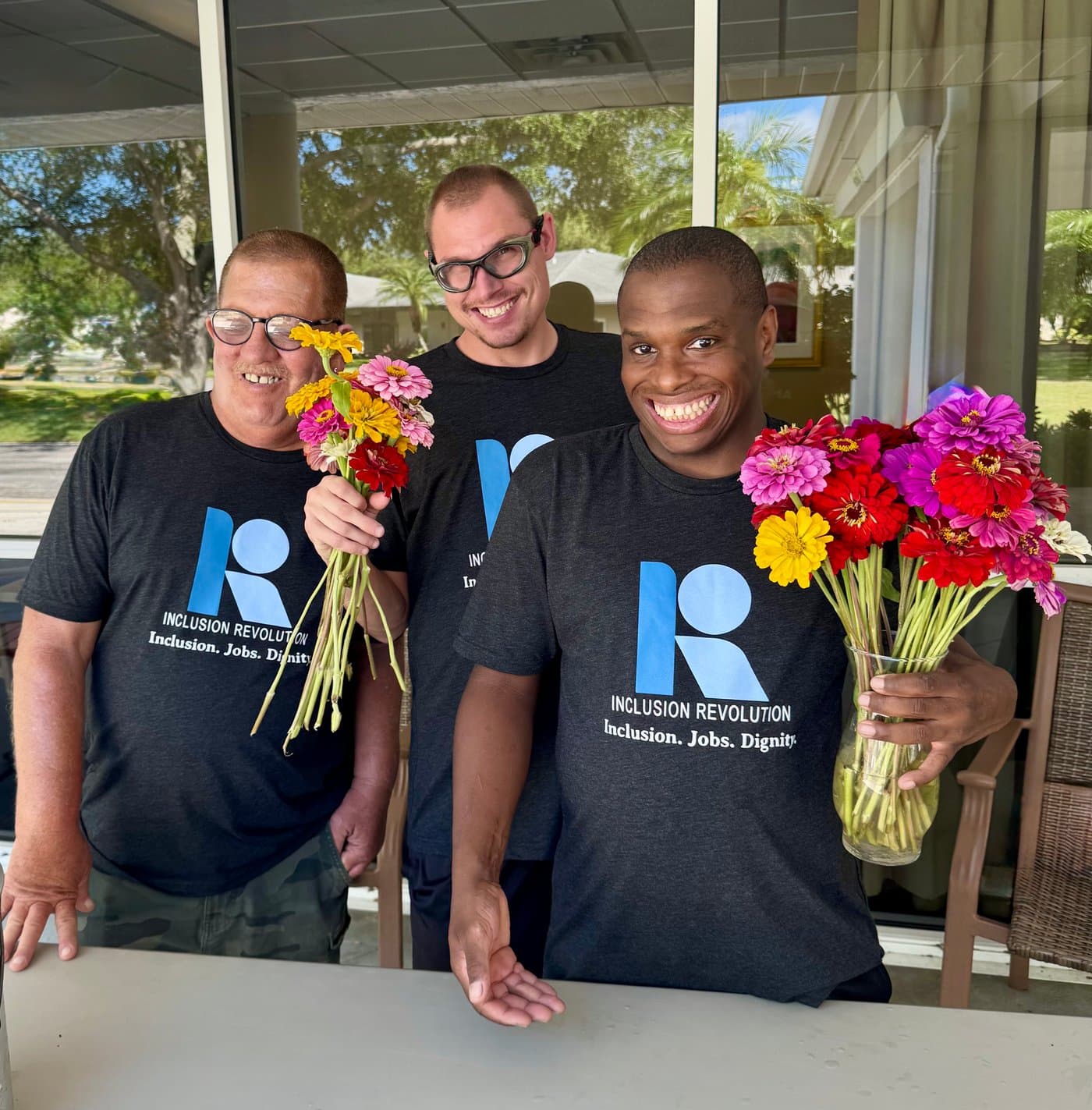 Three Inclusion Revolution community members holding colorful flowers